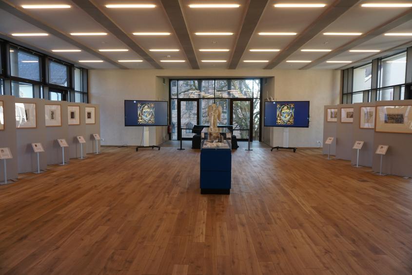 Ein Blick in die Ausstellung. Zentral der Posaunenengel aus Gips, rechts und links Stellwände mit den gerahmten Aquarellen von Fritz Geiges.